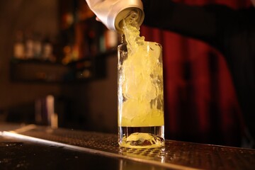 Bartender pouring energy drink into glass at counter in bar, selective focus
