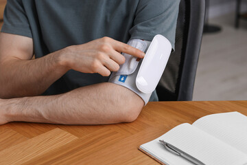 Fototapeta premium Man measuring his blood pressure with tonometer at wooden table indoors, closeup