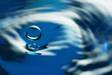 Splash of clear water with drop on blue background, closeup