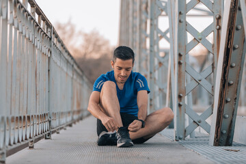 Young athlete sitting on the ground tying his laces on an iron bridge, sports concept.