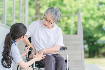 車椅子に乗る股関節が痛い高齢者と介護士の女性（リウマチ・人工関節）
