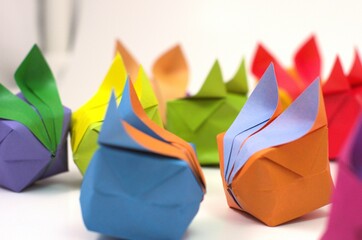 Side view of two small origami rabbits facing towards each other as if seeing each other for the first time, surrounded by other bunnies, against a white backdrop.