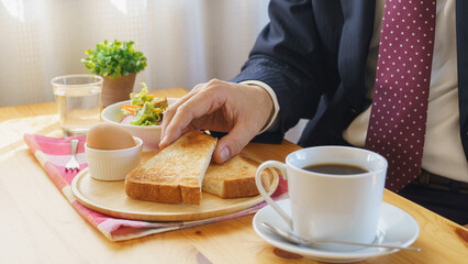 朝食を食べるビジネスマン｜コーヒー・トースト・ゆで玉子・サラダのモーニングセット　イメージ