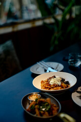 Eggplant pasta, onsen eggs, spiced chicken wings, fried food, restaurant food, casual entertainment, wooden tabletop, background, white ceramic plate, metal saucer, dipping sauce