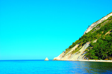 Fototapeta premium Crisp scenery with Mount Conero and Scoglio della Vela, the sail-shaped rocky formation rising from a bed of candid Adriatic Sea waters, azure, emerald, sparkling and mirroring, under a clear sky