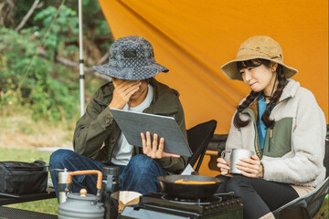 秋冬のキャンプ場でタブレットPCを見ながらキャンプをする男女のキャンパー（Wi-Fi・電源サイト）
 - obrazy, fototapety, plakaty