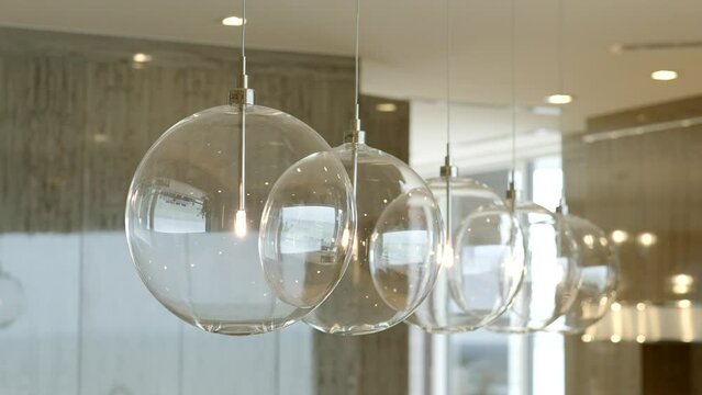 Transparent round lamps in form of balls hanging on suspended ceiling in row with warm shade lightning on blurred background of contemporary designed apartment