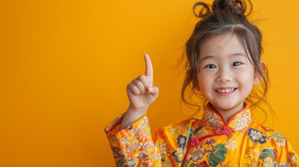5 year old girl in a fresh and neat cheongsam Smiling brightly as he pointed up and to the right. With a bright yellow backdrop. It adds a delightful touch. - obrazy, fototapety, plakaty