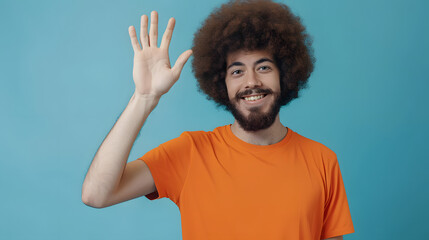 Fototapeta na wymiar Portrait of cheerful friendly man with Afro hairstyle wearing orange T-shirt saying hi and waving hand, greeting, looking at camera. Indoor studio shot isolated on blue background.