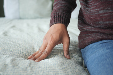 Hand touching and pressing orthopedic mattress on bed.