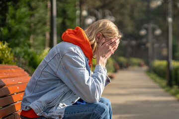 Upset sad hipster guy sitting on bench, hiding face with hands, crying. Unhappy male feeling...