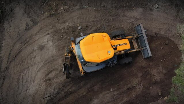 Yellow digger moves soil around on a plot of land, clearing to build