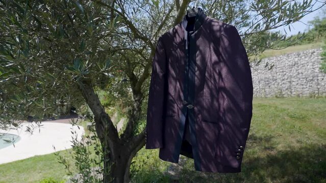 Slow orbiting shot of a the grooms wedding suit hanging on a tree in the garden