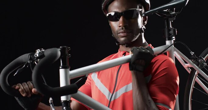 Focused African American cyclist holding a bicycle on a black background
