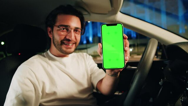 Man Driver holding Phone with Chroma Key close-up. Car Sharing concept, Vehicle and Transport. Young Guy Driving, showing Green Screen on Smartphone. Traveling by Automobile. 
