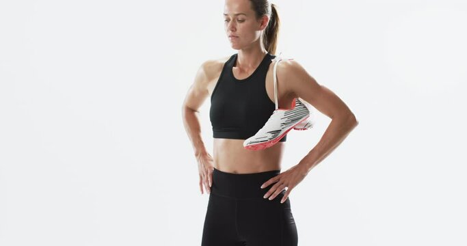 Young Caucasian woman athlete holds running shoes on a white background