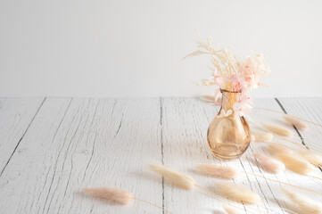 Vintage style of pastel natural colored, beige, and pink foxtail and dried flower in a vase against a white wooden backdrop with space for text. Spring and Autumn inspiration