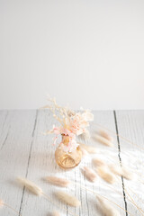 Vintage style of pastel natural colored, beige, and pink foxtail and dried flower in a vase against a white wooden backdrop with space for text. Spring and Autumn inspiration
