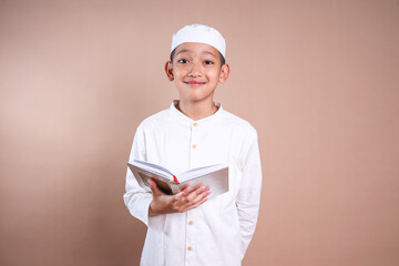 Young Asian Muslim boy wear skullcap holding holy book of Quran 