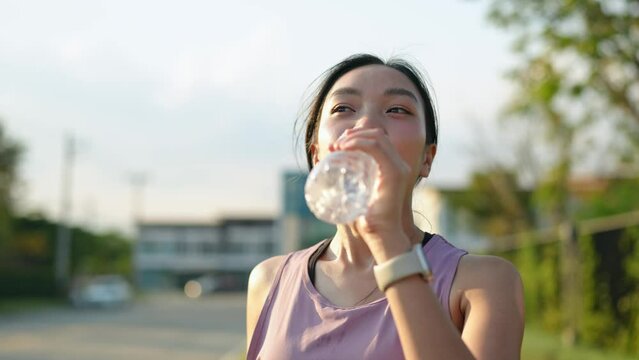 Confident young Asian woman running outdoors along the village street. Stand and drink water to cool down. healthy lifestyle and sports concepts Use your free time to your advantage.