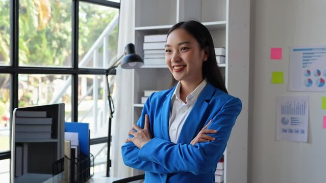 Asian businesswoman stands with her arms crossed, smiling in confidence, putting together her work in a recording plan. financial goals online business and chronicles the career wishes of success.