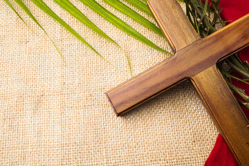 Jesus Wooden cross with palm leaves, red cloth and Crown of Thorns. Catholic Christians Good Friday Ceremony. Isolated on brown burlap fabric background with empty blank copy text space. - obrazy, fototapety, plakaty