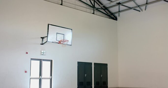 An indoor basketball hoop is mounted on a white wall in a gymnasium