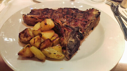 A hearty meal of grilled pork ribs with a side of roasted potatoes served on a white plate,...