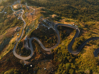 Aerial view of serpentine roads slicing through the rugged terrain of a mountain, illuminated by the warm glow of the setting sun.