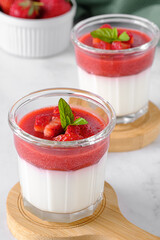 Two glasses with traditional italian dessert panna cotta with strawberries on light background. Gluten-free vegetarian food.
