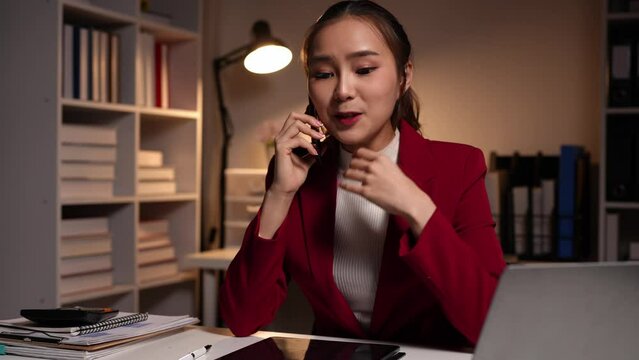 Asian businesswoman, customer sales manager of a busy company while talking on the phone with customers. Looking at documents, files, financial details, agreements, and contracts in the office.