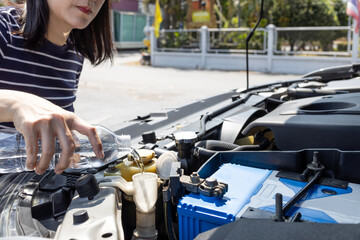 Asian woman pouring clean water from bottle into the windshield washer fluid tank of a car,female filling the windshield washer fluid,check liquid level in reservoir at engine room,maintenance concept