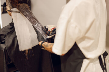 Close up of colorist dyes hair of woman with brush and foil in beauty salon