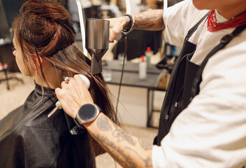 Close up of professional female barber with hair dryer and brush styling hair of customer in salon