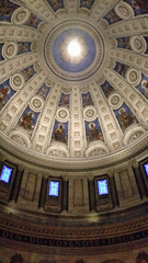 The ornate dome interior of a grand building with elaborate frescoes, coffered detailing, and...