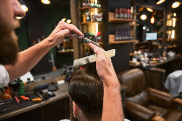 Close-up photo of barber cutting wet hair. Professional hairdresser making fresh hairstyle. Back view of man getting new haircut.