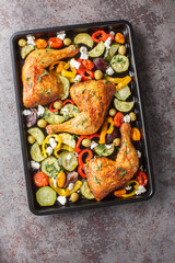 Baked chicken legs with zucchini, tomatoes, peppers, olives and feta cheese close-up on a baking sheet on the table. Vertical top view from above