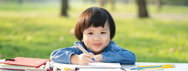 asian little girl drawing on paper in garden.