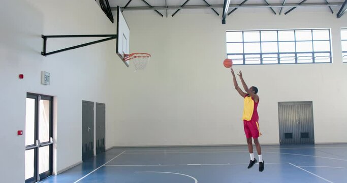 A basketball player shoots for the hoop in an indoor court