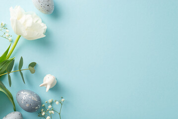 Easter motif visual with top view of slate greyish eggs, a small bunny sculpture, gypsophila, tulip, and eucalyptus branch set against a pastel blue canvas, leaving space for words