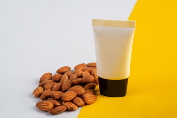 Cosmetic product in tube, bottle, lotion or serum with almonds seed on yellow and white background. 