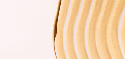 creamy cosmetic texture of golden shining color cosmetic smear on a light background close-up