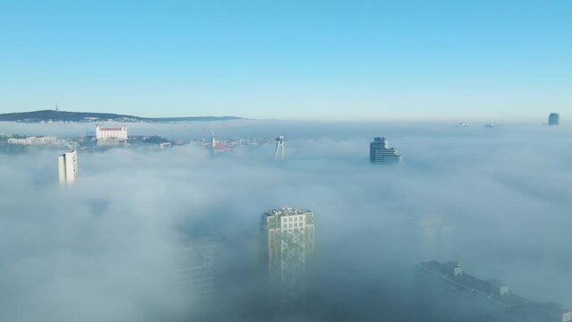 A sunlit aerial adventure unfolds as a drone moves forward, capturing the Bratislava castle and buildings emerging through dense inversion clouds. Cinematic allure of urban exploration. LuPa Creative.