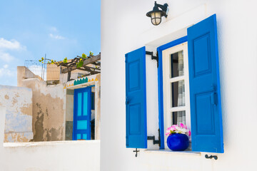 Window with blue shutters and flower. White architecture in Santorini island, Greece.
