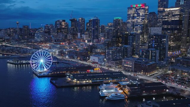 Aerial panorama of seafront and financial district skyscrapers and buildings, downtown Seattle at dark winter night light. 4K b roll drone shot of cityscape night scene. Illuminated night city USA