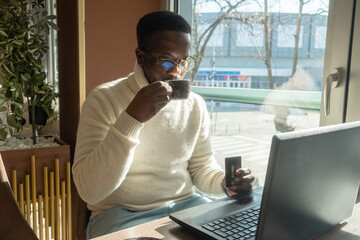 Young black man businessman buying online with a credit card and a laptop on the internet and...