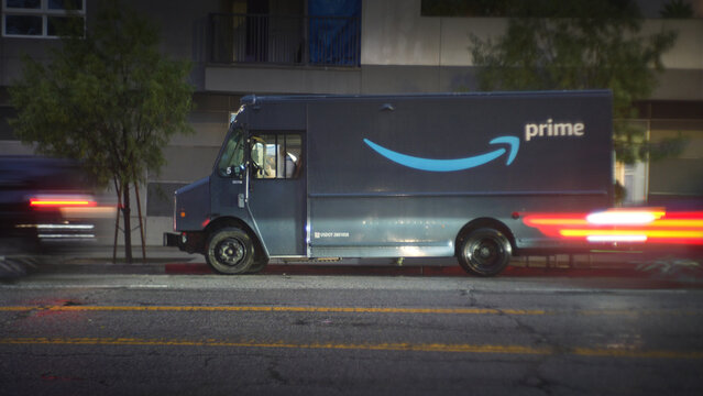 LOS ANGELES, CA - February 19, 2024: Amazon Prime delivery truck delivering packages to a building on a busy street at night in rush hour traffic.