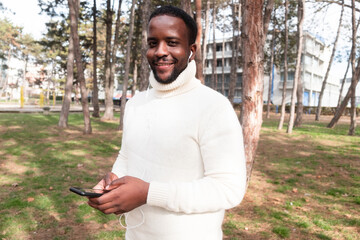 Young black man yuppie hipster in a park using a mobile phone and smiles