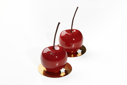 Two cherry-shaped desserts with red glaze and chocolate stems