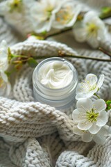 Fototapeta na wymiar Creamy face cream in jar with blooming branches on knitted background